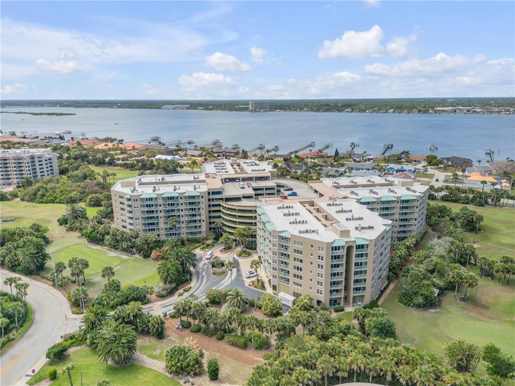An aerial view shows a large multi-story apartment complex surrounded by green lawns and water — 4 OCEANS WEST BOULEVARD UNIT 402A, DAYTONA BEACH, FL