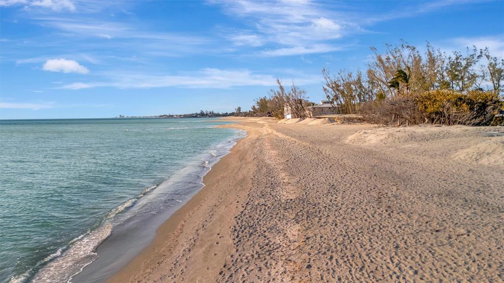 A sandy beach stretches along the coastline with sparse trees and a distant building — 8555 HERON LAGOON CIRCLE, SARASOTA, FL