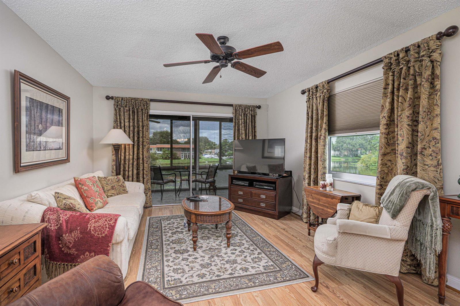 A living room with wood flooring, a ceiling fan, a television, and a sliding glass door — 1225 NW 21st Street # 708, Stuart FL 34994, STUART, FL