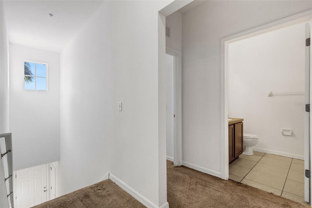A carpeted hallway leads to a bathroom with a vanity and tile flooring — 5328 MANG PLACE UNIT 1305, SARASOTA, FL