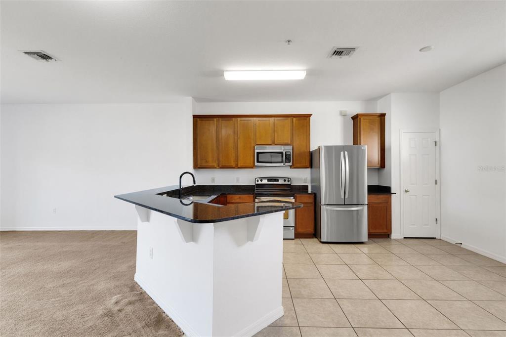 A kitchen features wood cabinets, stainless steel appliances, a granite island, and tile flooring — 5328 MANG PLACE UNIT 1305, SARASOTA, FL