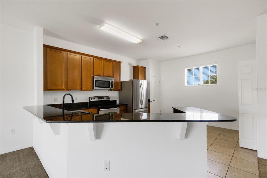 A kitchen features wood cabinets, stainless steel appliances, and a black granite breakfast bar — 5328 MANG PLACE UNIT 1305, SARASOTA, FL