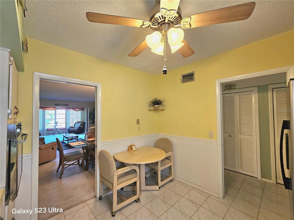 A kitchen dining area features yellow walls, white wainscoting, tile flooring, and a ceiling fan — 2440 WORLD PARKWAY BOULEVARD UNIT 46, CLEARWATER, FL