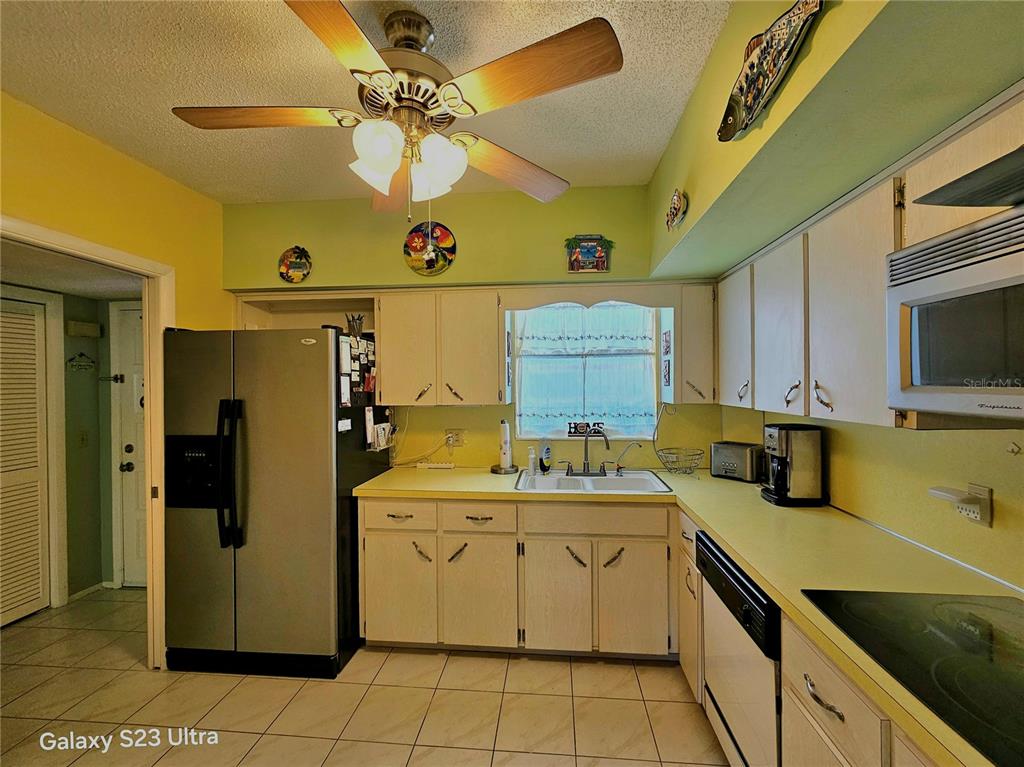 A kitchen features light-colored cabinets, yellow countertops, a stainless steel refrigerator, and a ceiling fan — 2440 WORLD PARKWAY BOULEVARD UNIT 46, CLEARWATER, FL