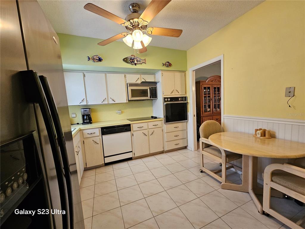 A kitchen with white cabinets, stainless steel appliances, tile flooring, and a dining table — 2440 WORLD PARKWAY BOULEVARD UNIT 46, CLEARWATER, FL