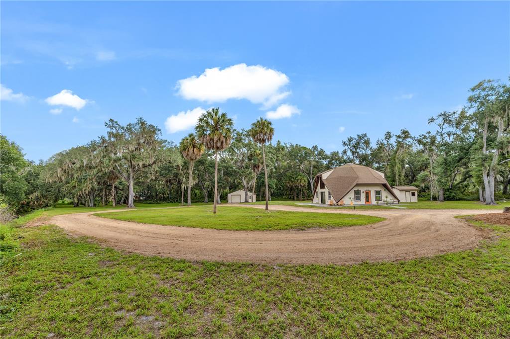 A geodesic dome house sits on a grassy lot with a dirt driveway and palm trees — 1213 BUTCH CASSIDY TRAIL, WIMAUMA, FL