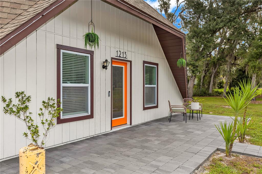 A white A-frame house features a bright orange front door and a gray paver patio — 1213 BUTCH CASSIDY TRAIL, WIMAUMA, FL