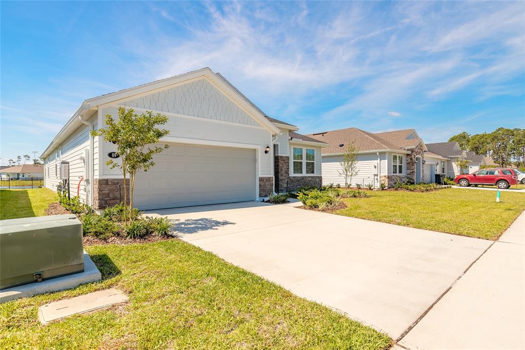 A light-colored suburban house with a two-car garage and stone accents on a sunny day — 89 SIGNET CIRCLE, FLAGLER BEACH, FL