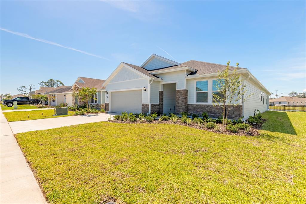 A single-story suburban house with a two-car garage, stone accents, and a landscaped front yard — 89 SIGNET CIRCLE, FLAGLER BEACH, FL