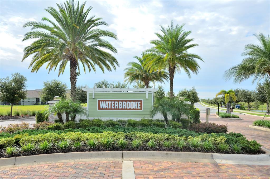 A sign reading Waterbrooke stands in front of palm trees and a paved entrance road — 2331 GARDEN BELLE DRIVE, CLERMONT, FL