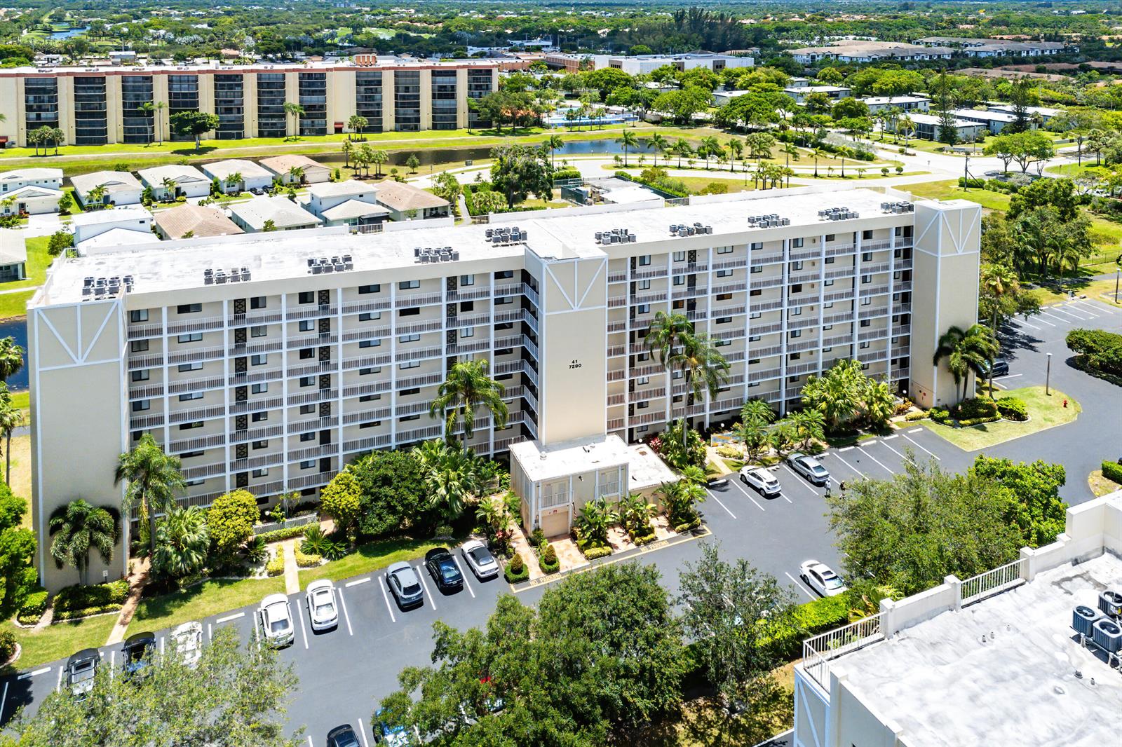 An aerial view shows a multi-story apartment building with a parking lot and landscaping — 7290 Kinghurst Drive # 607, Delray Beach FL 33446, DELRAY BEACH, FL
