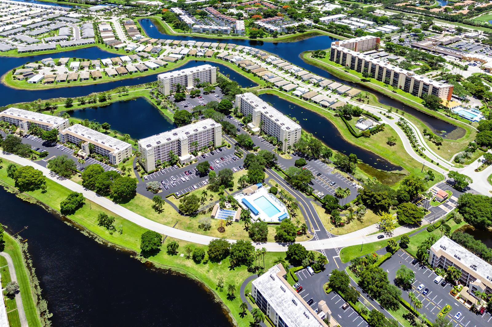 Aerial view of a residential complex with multiple apartment buildings, a swimming pool, and canals — 7290 Kinghurst Drive # 607, Delray Beach FL 33446, DELRAY BEACH, FL