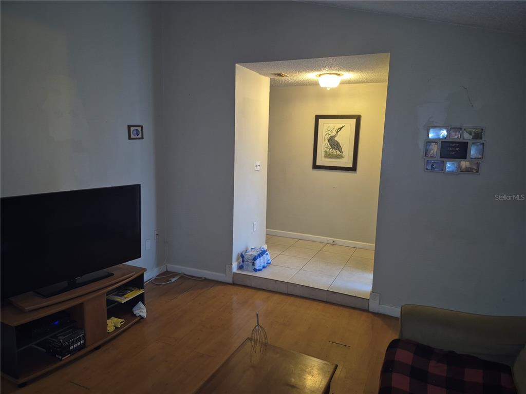 A living room with wood flooring, a television console, and an opening to a tiled area — 13710 WHITBY ROAD, HUDSON, FL