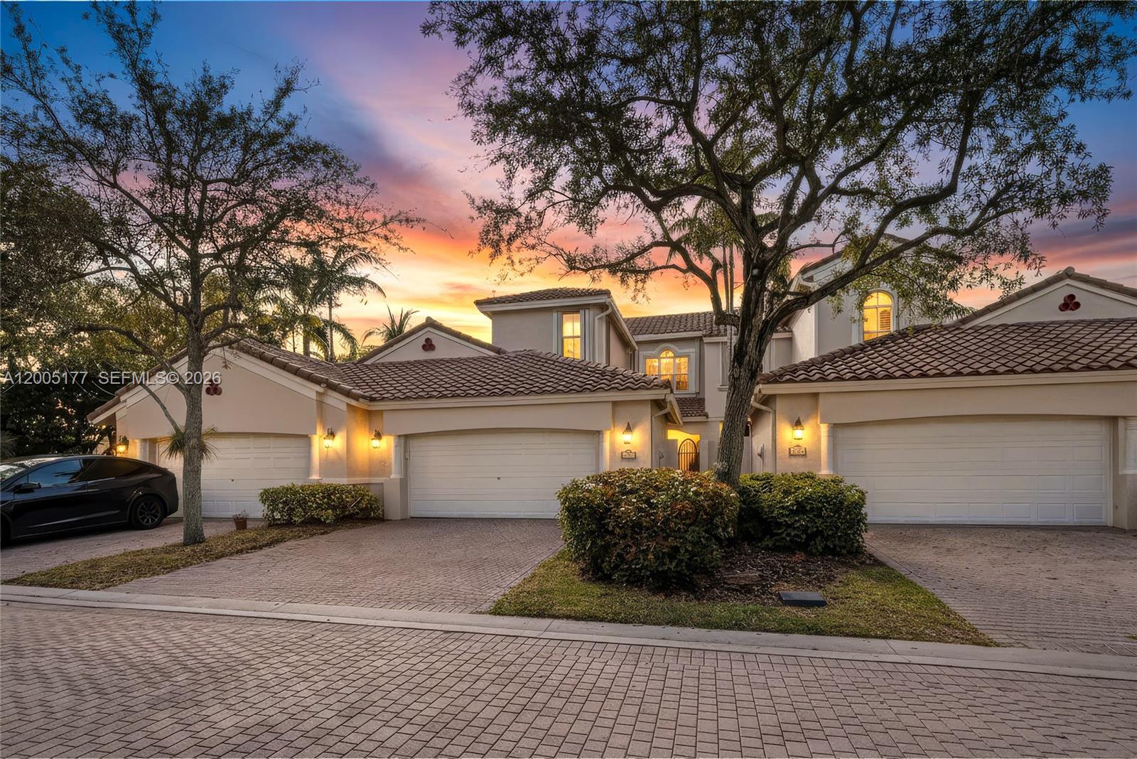 A multi-car garage house exterior features a paved driveway and mature trees at sunset — 1366 W Harbor Vw W, Hollywood FL 33019, HOLLYWOOD, FL
