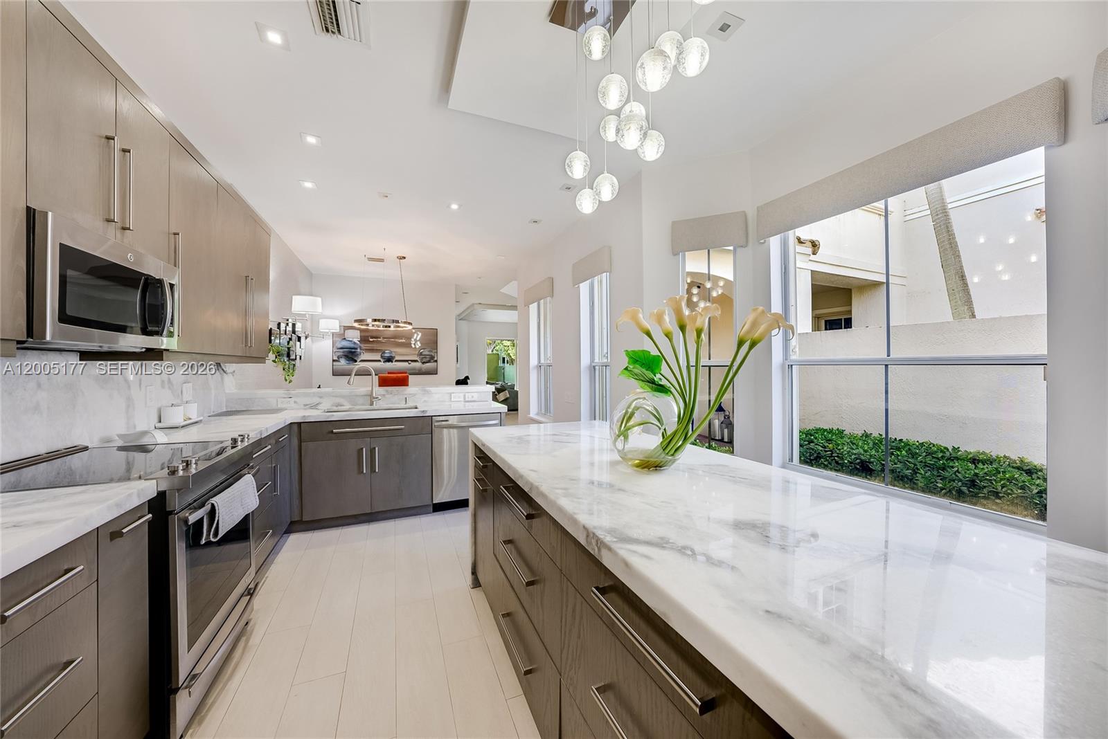 A modern kitchen features dark wood cabinetry, marble countertops, and a large central island — 1366 W Harbor Vw W, Hollywood FL 33019, HOLLYWOOD, FL