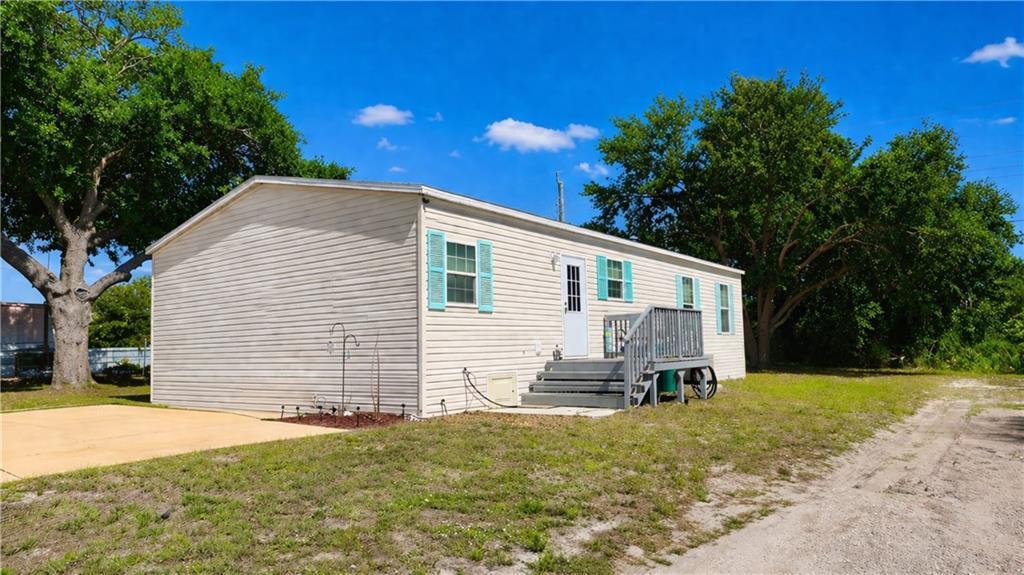 A single-story mobile home with light siding, blue shutters, and a wooden deck entrance — 324 Valencia Street, Sebastian FL 32958, SEBASTIAN, FL