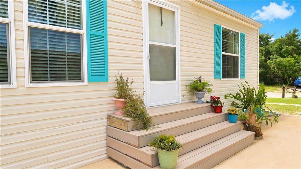 A beige mobile home exterior features a wooden staircase with potted plants and turquoise shutters — 324 Valencia Street, Sebastian FL 32958, SEBASTIAN, FL
