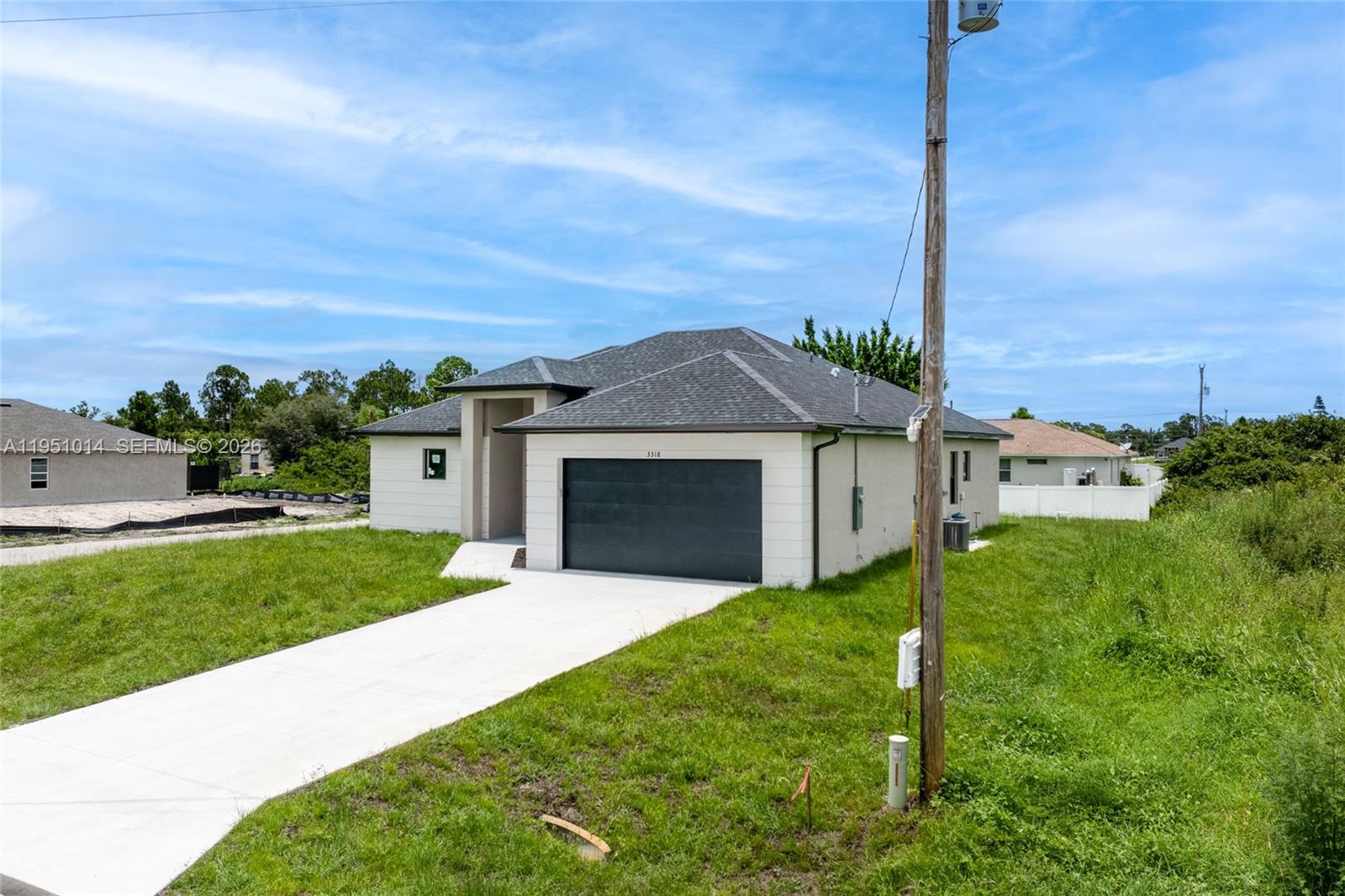 A single-story house with a dark garage door and a concrete driveway sits on grass — 3318 30th St SW, Lehigh Acres FL 33976, LEHIGH ACRES, FL