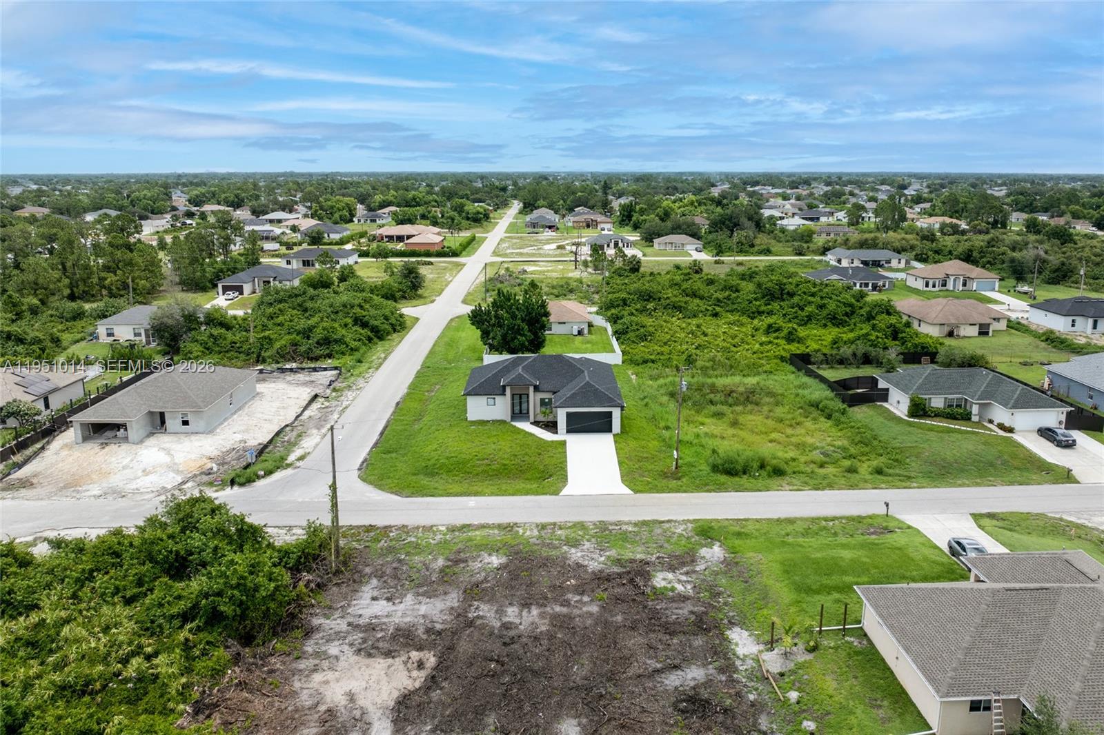 An aerial view shows a modern single-story house surrounded by undeveloped lots and suburban homes — 3318 30th St SW, Lehigh Acres FL 33976, LEHIGH ACRES, FL