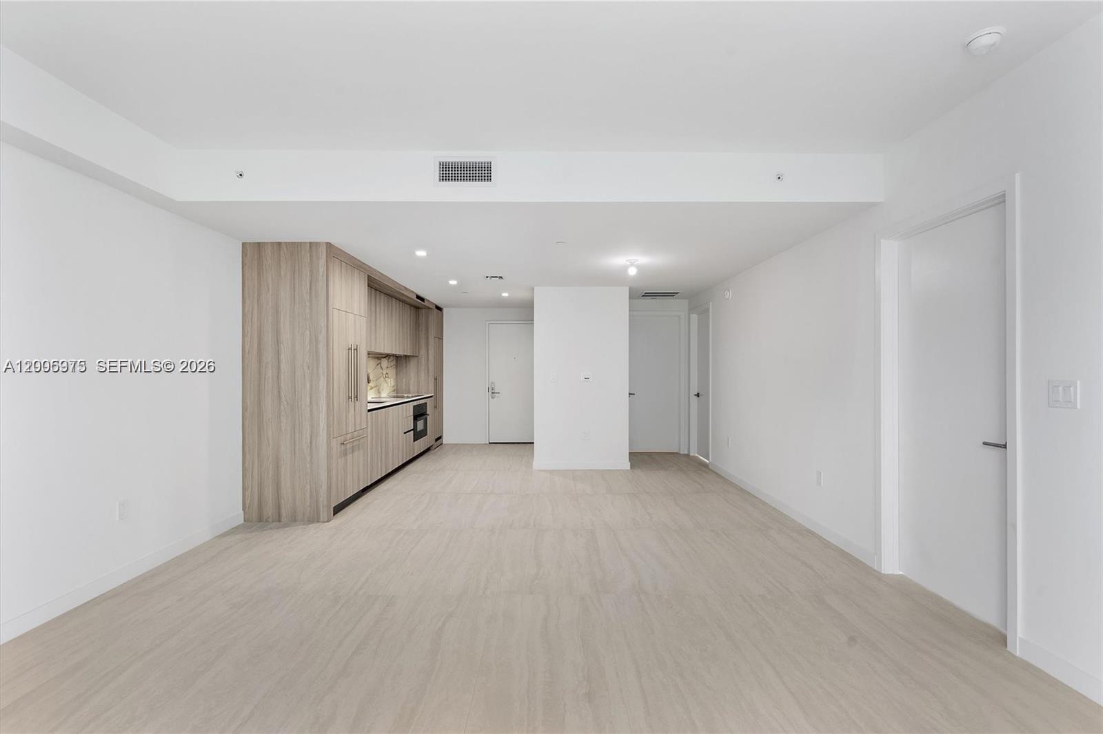 This minimalist open-plan living area features light wood-look flooring and a modern kitchen wall — 77 SE 5th St # 4106, Miami FL 33131, MIAMI, FL