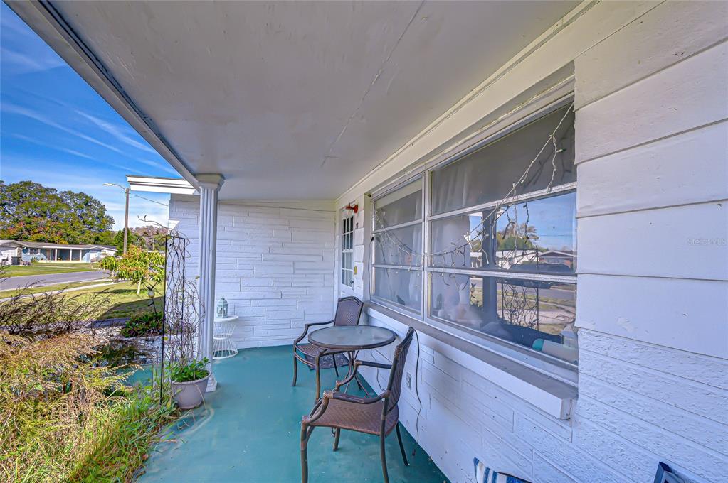 A covered front porch features white brick walls, a teal floor, and a small bistro set — 2128 SHANNON DRIVE, HOLIDAY, FL