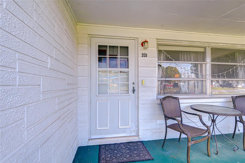 A white front door with a glass panel sits on a porch with patio furniture — 2128 SHANNON DRIVE, HOLIDAY, FL