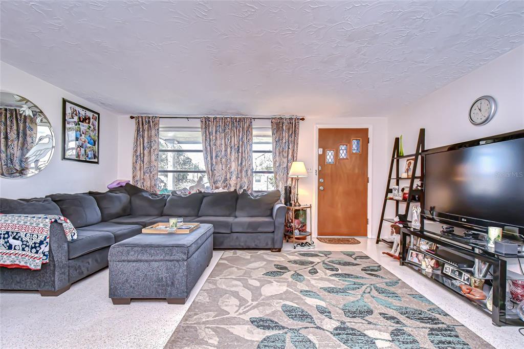 A living room features a large gray sectional, an ottoman, a patterned rug, and television — 2128 SHANNON DRIVE, HOLIDAY, FL