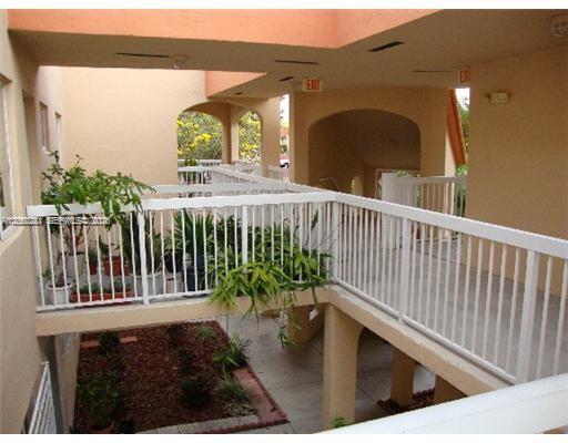 An elevated outdoor walkway with white railings overlooks a small garden area below — 2390 W 74th St # 202, Hialeah FL 33016, HIALEAH, FL