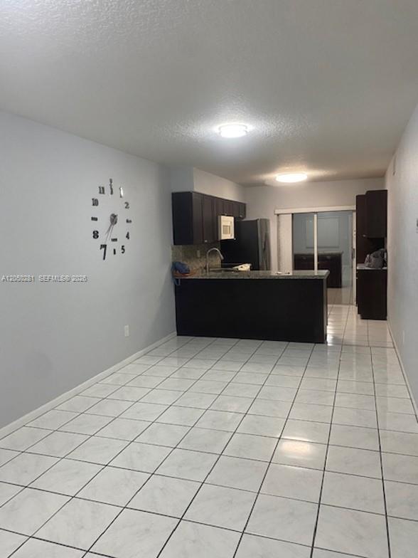 An open-concept kitchen features dark wood cabinets, granite countertops, and white tiled flooring — 2390 W 74th St # 202, Hialeah FL 33016, HIALEAH, FL