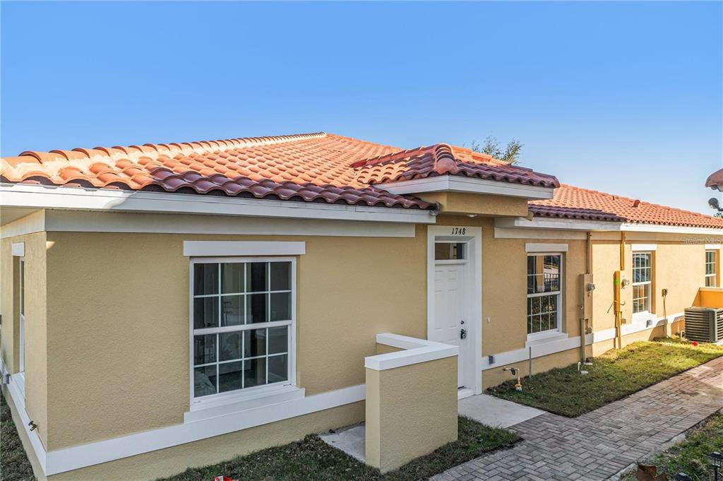 A single-story house exterior with yellow stucco walls, a tiled roof, and a brick walkway — 1793 CORIANDER DRIVE, POINCIANA, FL