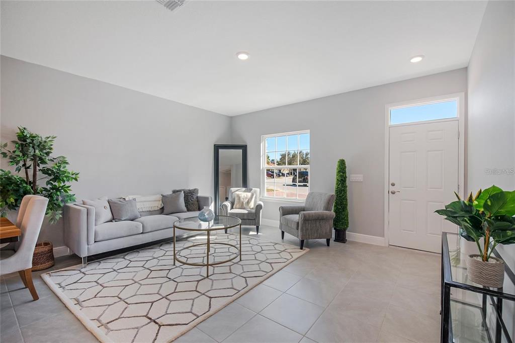 A living room features a gray sofa, two armchairs, a geometric rug, and a front door — 1793 CORIANDER DRIVE, POINCIANA, FL