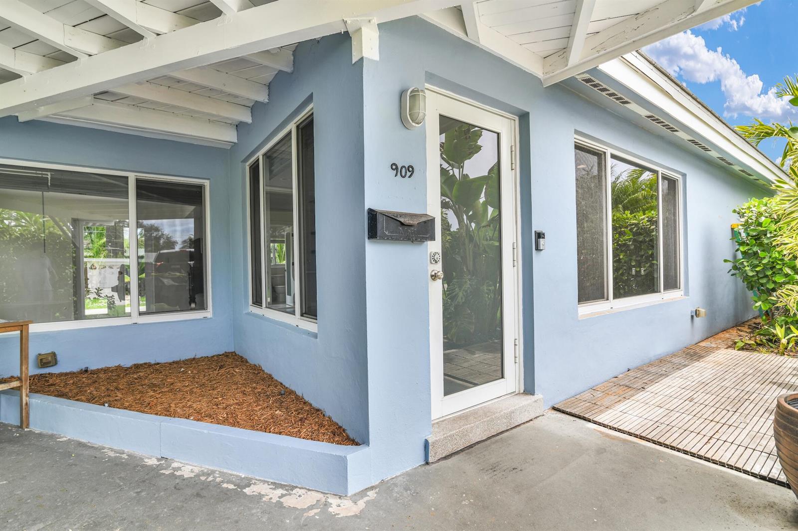 The exterior of a light blue house features a front door, windows, and mulch bed — 909 SE 16 Place, Deerfield Beach FL 33441, DEERFIELD BEACH, FL