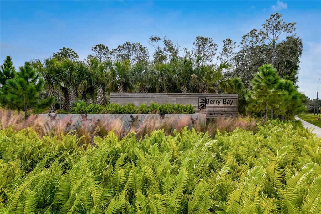 A wooden sign reading Berry Bay stands behind lush green ferns and ornamental grasses — 4916 MEADOW BAY COURT, WIMAUMA, FL