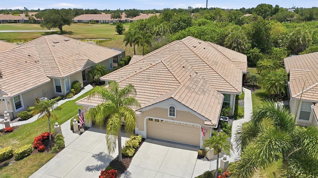 An aerial view shows a tan house with a tiled roof, garage, and palm trees — 1808 SAN TROVASO WAY, VENICE, FL