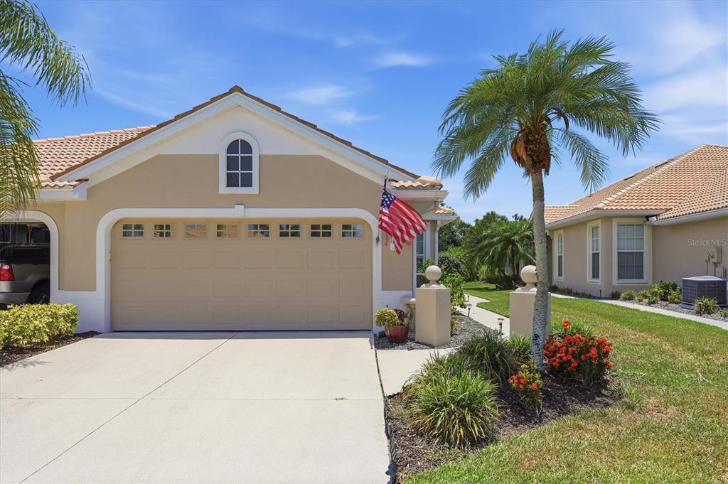 A tan house exterior features a two-car garage, a palm tree, and an American flag — 1808 SAN TROVASO WAY, VENICE, FL