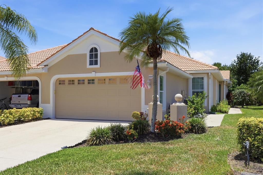 A single-story house with a tan stucco exterior, a two-car garage, and a palm tree — 1808 SAN TROVASO WAY, VENICE, FL