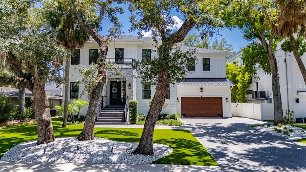 A two-story white house with a stone entryway, a wooden garage door, and mature trees — 4814 W SAN JOSE STREET, TAMPA, FL