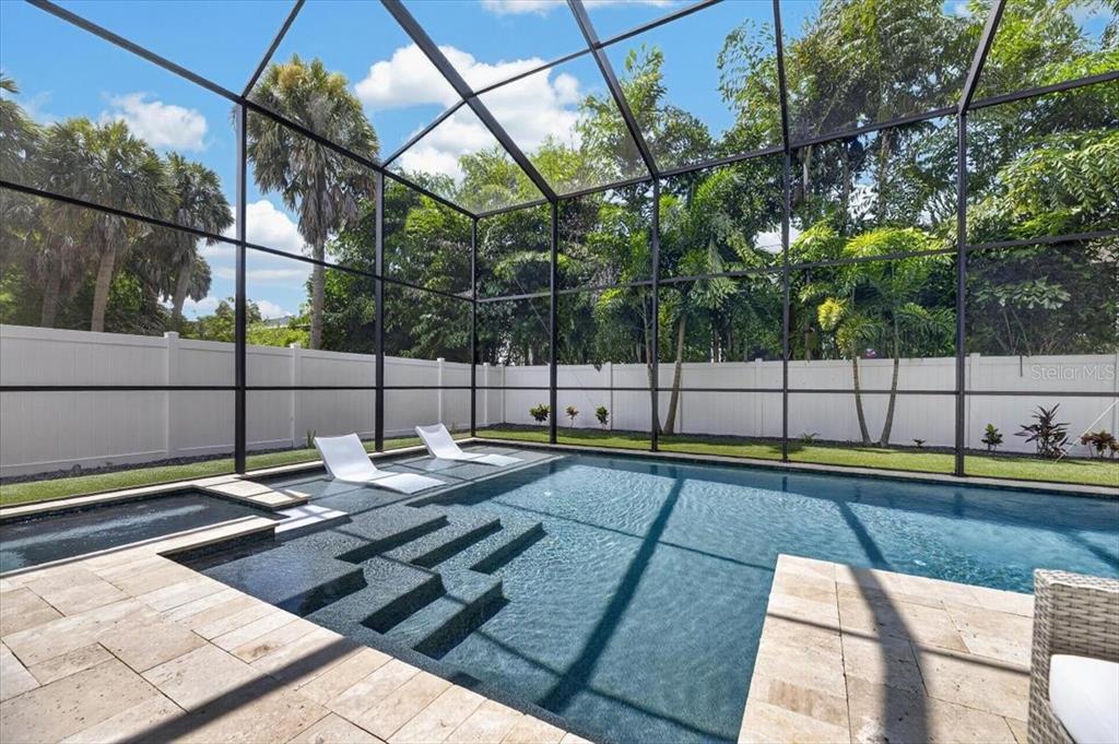 A screened-in swimming pool with a sun shelf, lounge chairs, and a white privacy fence — 4814 W SAN JOSE STREET, TAMPA, FL