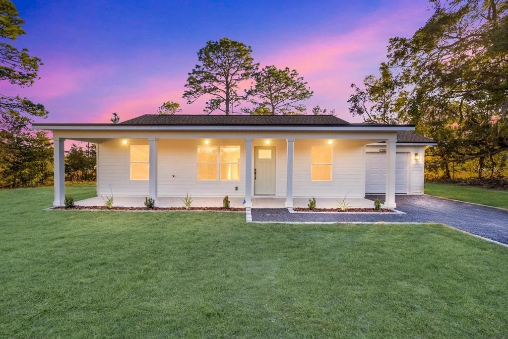 A white single-story house with a covered front porch and a paved driveway at dusk — TBD SEQUOIA LOOP DRIVE, OCKLAWAHA, FL