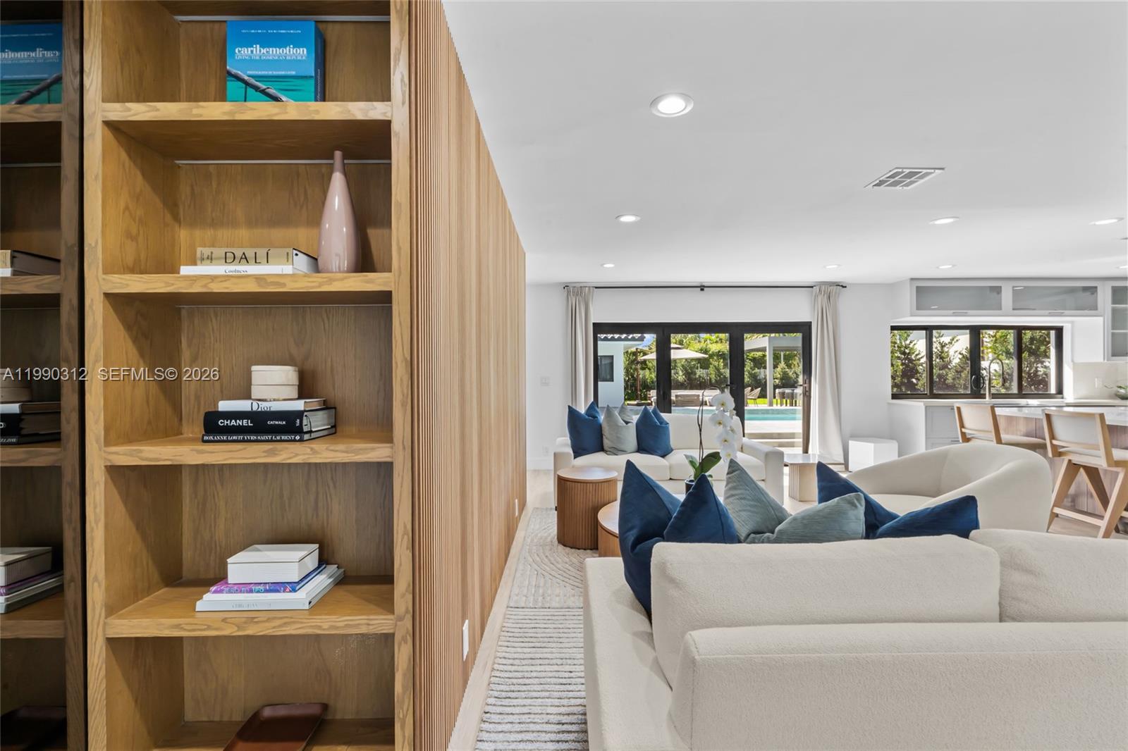 A modern living room features a slatted wood shelving unit, white sofas, and a pool view — 116 W 1st Ct, Miami Beach FL 33139, MIAMI BEACH, FL