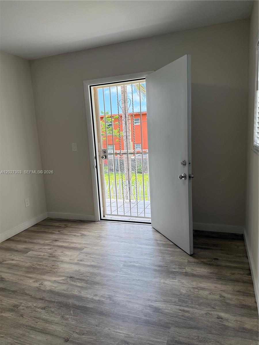 A room with wood-look flooring features an open door leading to a gated exterior — 1580 SW 2nd St # 4, Miami FL 33135, MIAMI, FL