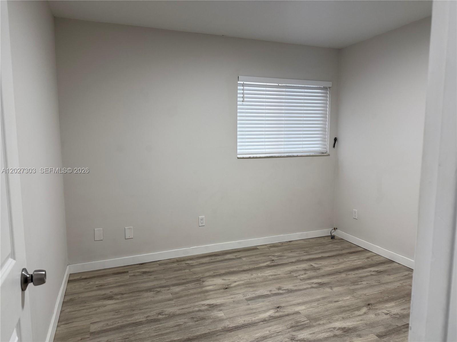 An empty room features light gray walls, wood-look laminate flooring, and a single window — 1580 SW 2nd St # 4, Miami FL 33135, MIAMI, FL