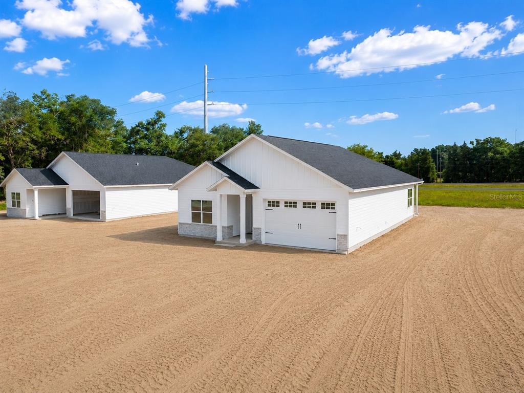 Two newly constructed white houses with dark roofs stand on a large, sandy lot — 13305 NE 54TH STREET, WILLISTON, FL