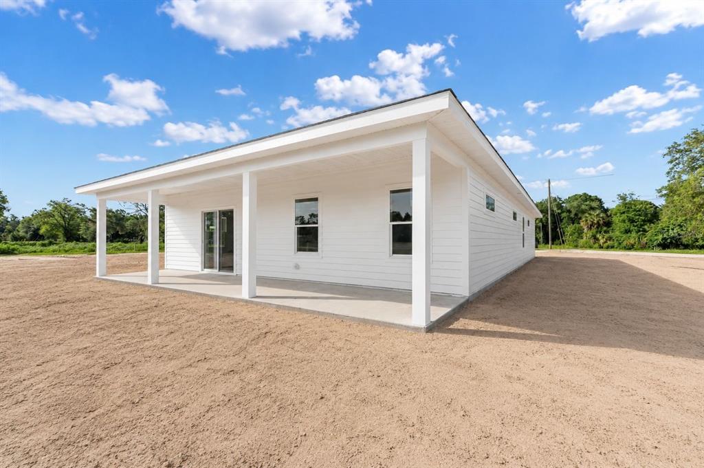 A white house with a covered porch and sliding glass doors sits on a dirt lot — 13305 NE 54TH STREET, WILLISTON, FL