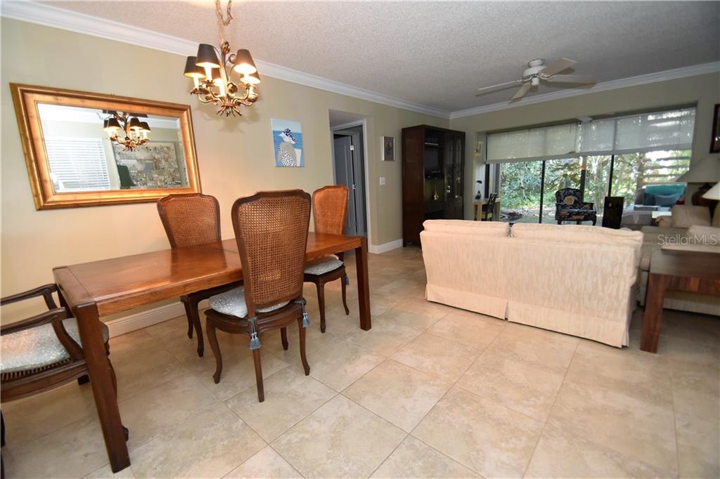 A dining area with a wooden table and chairs sits adjacent to a living room — 1716 GLENHOUSE DRIVE UNIT GL324, SARASOTA, FL