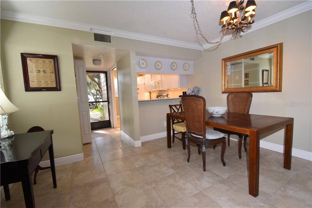 A dining room with tile floors, a wooden table, and a pass-through to the kitchen — 1716 GLENHOUSE DRIVE UNIT GL324, SARASOTA, FL