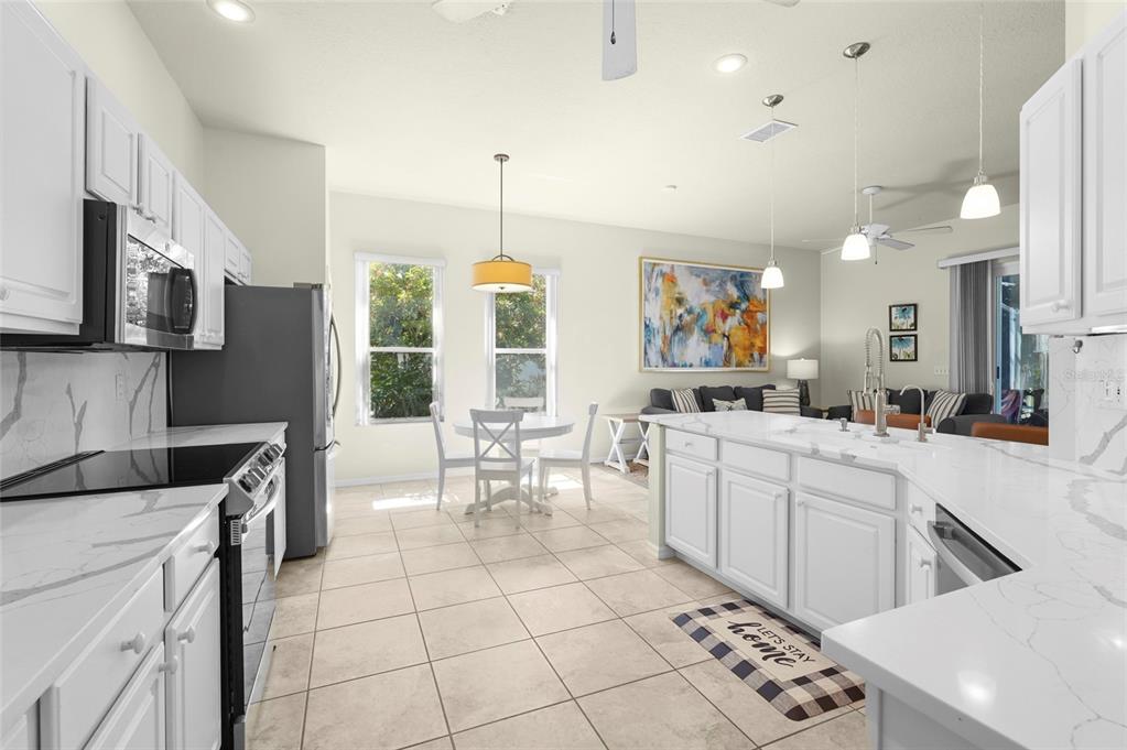 A bright open-concept kitchen features white cabinetry, marble-look countertops, and an island with seating — 4510 50TH DRIVE W, BRADENTON, FL