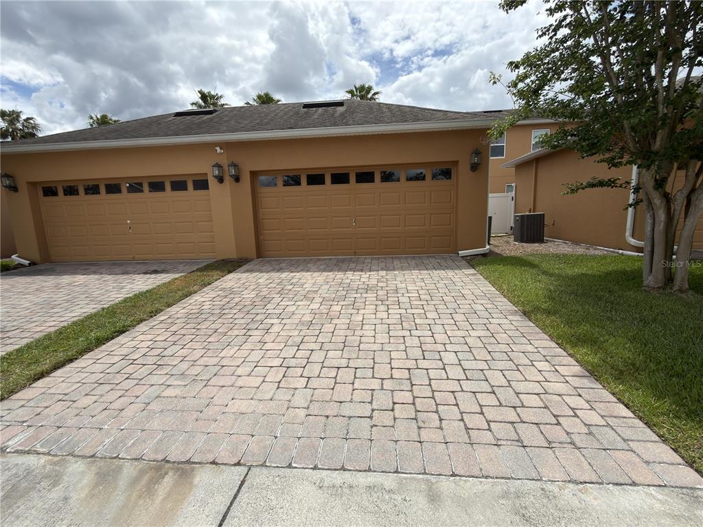 A two-car garage with tan stucco walls and a paved driveway — 5413 NEW INDEPENDENCE PARKWAY, WINTER GARDEN, FL