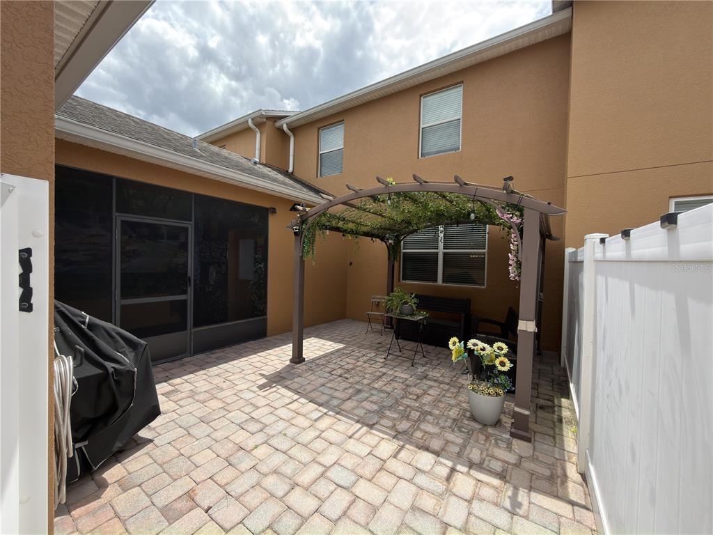 A paved patio features a metal pergola, outdoor seating, and a screened-in porch entrance — 5413 NEW INDEPENDENCE PARKWAY, WINTER GARDEN, FL