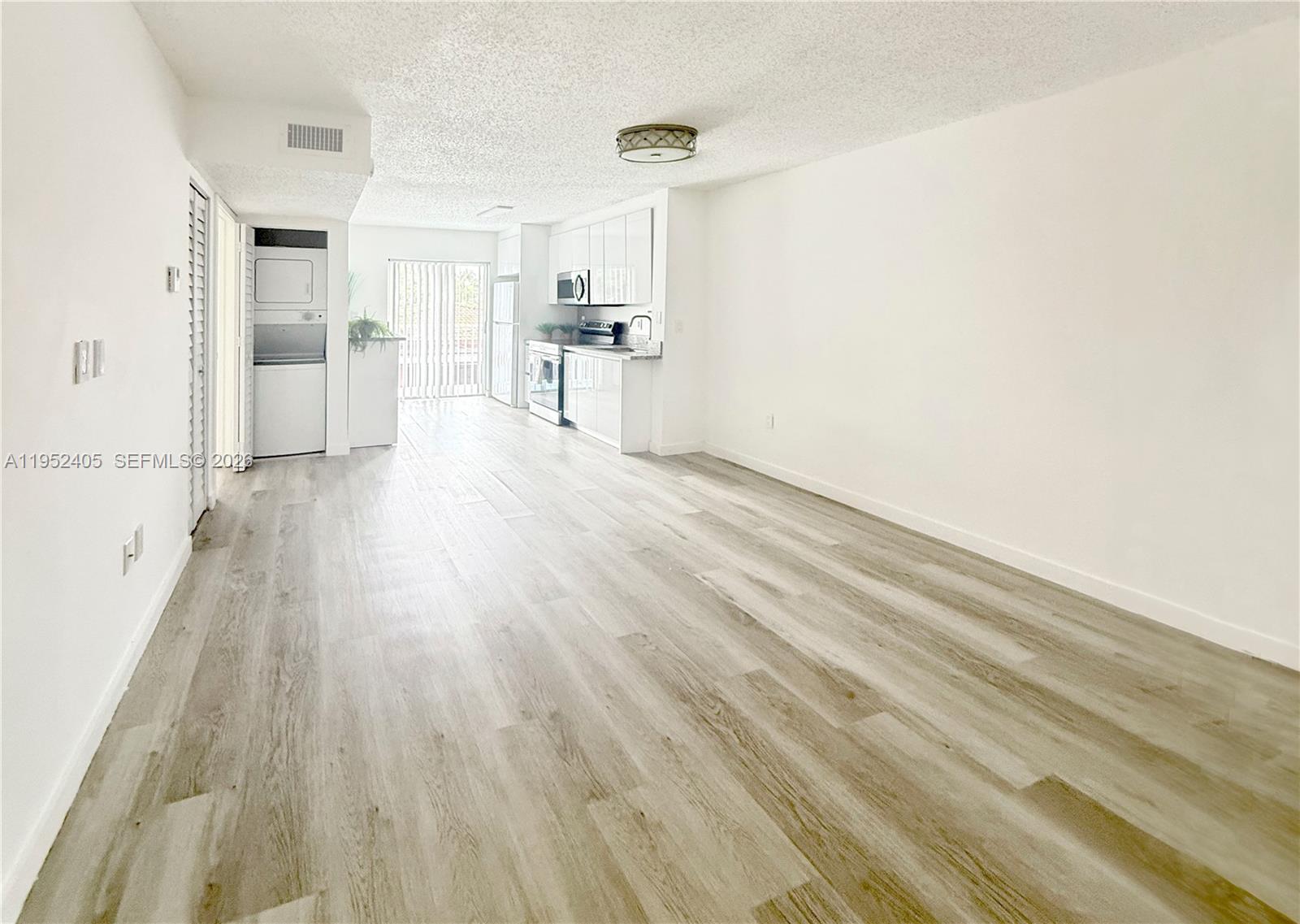 An open-concept living area features light wood-look flooring, white walls, and a modern kitchen — 2575 SW 27th Ave # 210, Miami FL 33133, MIAMI, FL